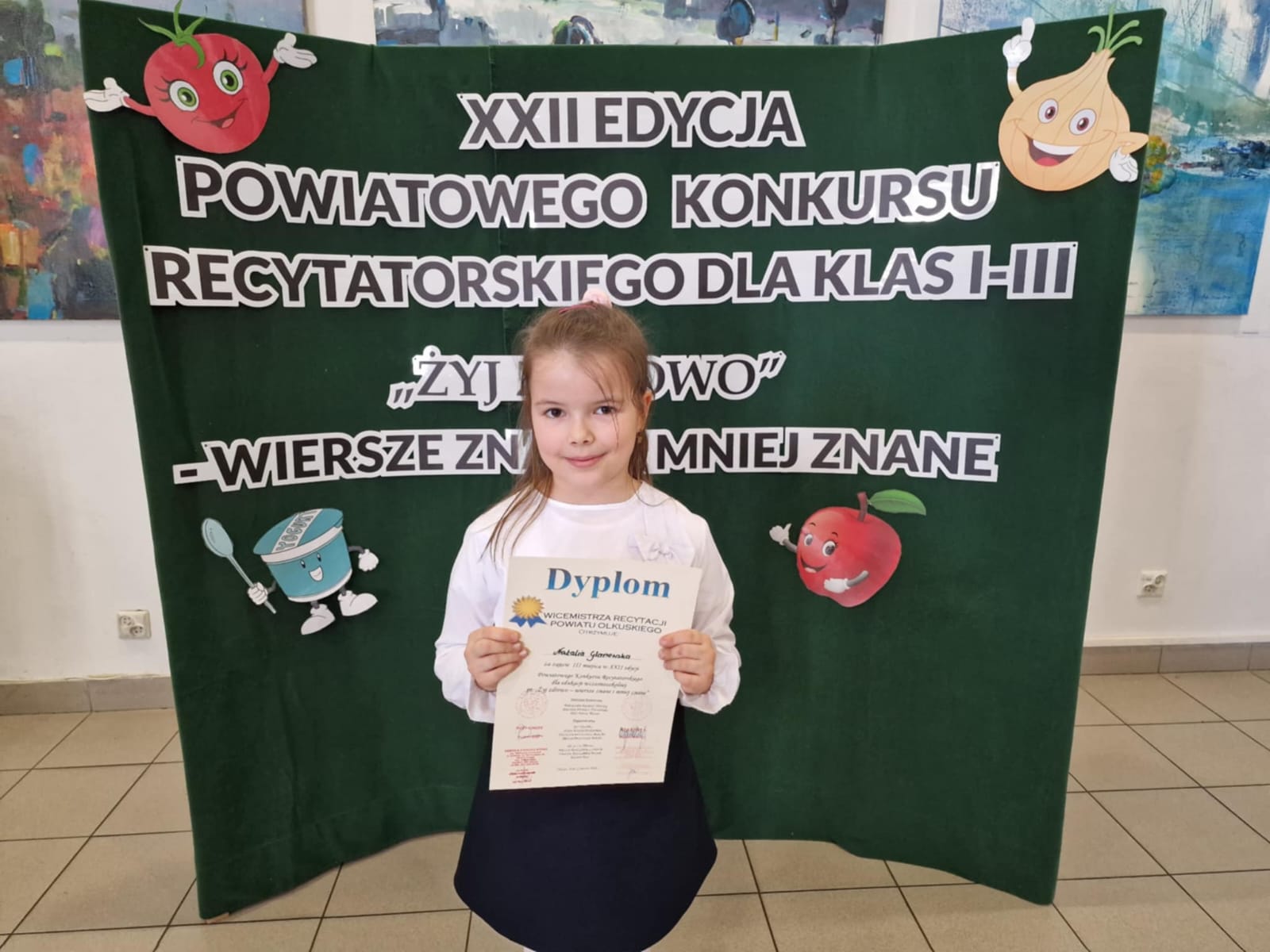 zwycięzca konkursu z dyplomem na tle banneru konkursowego